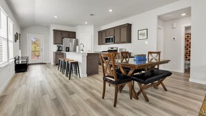 A modern kitchen with dark cabinets, a central island, and a dining area with wooden chairs and stools.