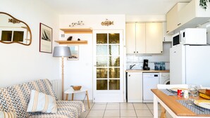 Un espace de vie compact comprenant un canapé, une table à manger, un coin cuisine et une porte dotée d’un panneau en verre.