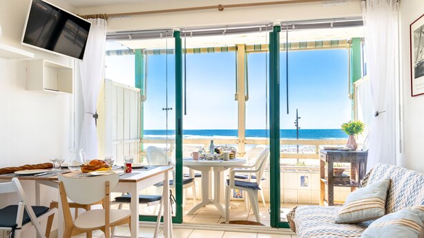 Une pièce comprenant une table à manger, des chaises, un canapé et donnant sur la plage.
