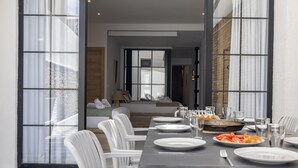 A dining area with a long table set for a meal, white chairs, and a view of a bedroom with a bed and a window. - My Loft 4 You Patraix Style (Valencia)