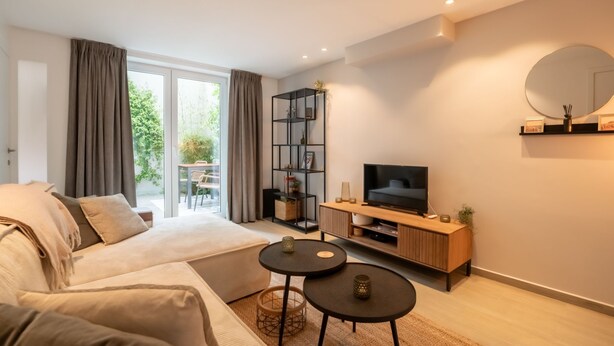 Una sala de estar moderna con sofá, televisor, estantería y comedor con mesa y sillas.