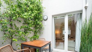 Un patio con mesa de madera y sillas de mimbre, rodeado de abundante follaje verde.