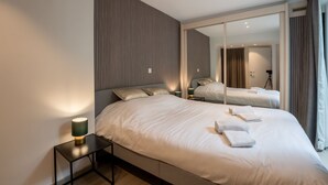 Habitación de hotel moderna con una cama grande, una mesita de noche con lámpara, un espejo y vistas al pasillo.