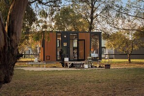 A modern, compact cabin with a wooden exterior, large windows, and a small porch area. - Ballarat Bliss by Tiny Away (Cardigan)