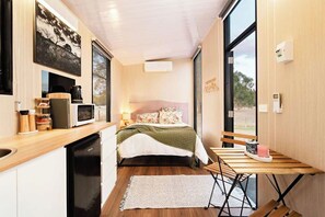 Een compacte slaapkamer met een bed, nachtkastje en een klein houten tafeltje met stoel.