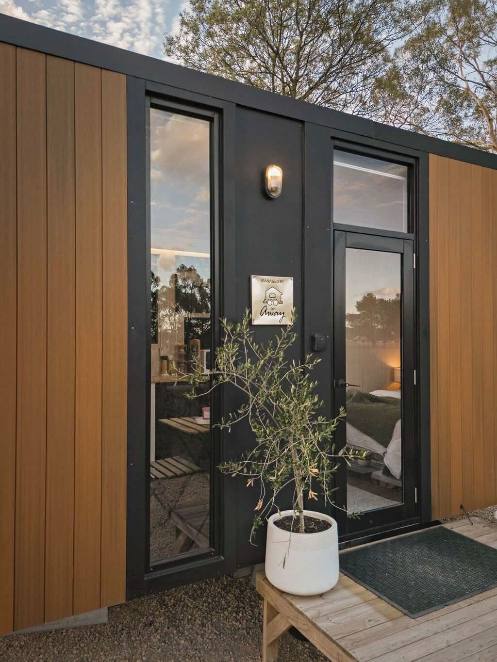 A modern building with a black exterior, large glass doors, and a small wooden table with a potted plant outside.
