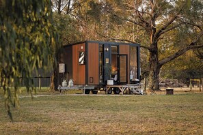 A modern, compact mobile home with a wooden exterior, a sliding door, and a small porch area. - Ballarat Bliss by Tiny Away (Cardigan)