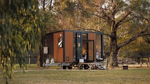 A modern, compact mobile home with a wooden exterior, a sliding door, and a small porch area. - Ballarat Bliss by Tiny Away (Cardigan)