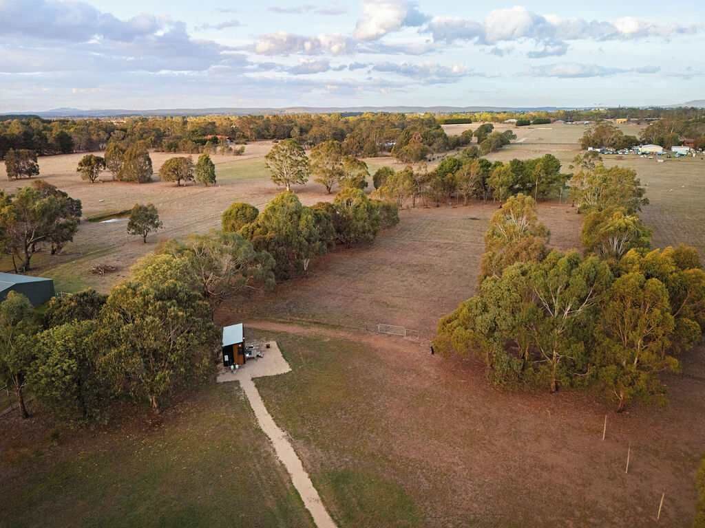 An aerial view of a rural property with a small cabin, surrounded by trees and open fields.