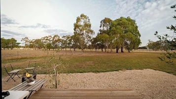 A wooden deck with a fire pit and seating area, surrounded by a grassy field and trees.