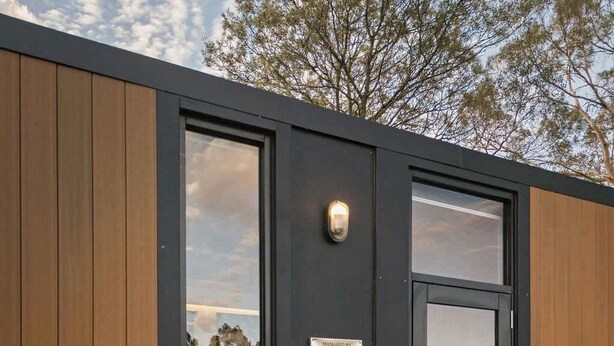 A modern building with a black exterior, large glass doors, and a small wooden table with a potted plant outside. - Ballarat Bliss by Tiny Away (Cardigan)
