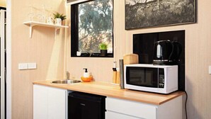 A compact kitchen with a wooden countertop, a white microwave, a coffee maker, and a window with a view of trees. - Ballarat Bliss by Tiny Away (Cardigan)
