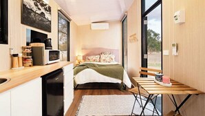 A compact bedroom with a bed, bedside table, and a small wooden table with a chair. - Ballarat Bliss by Tiny Away (Cardigan)