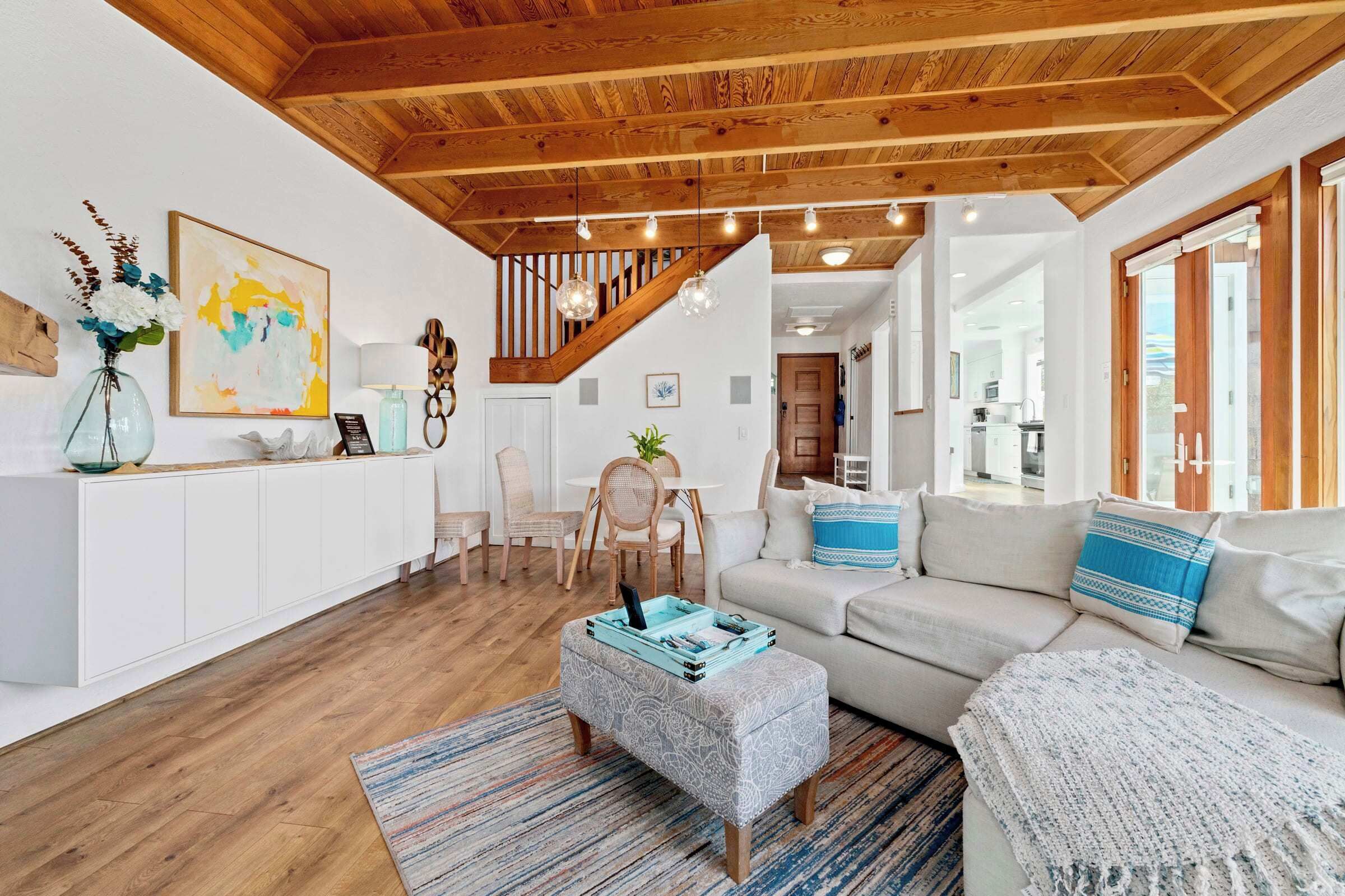 A spacious living area with a wooden ceiling, a staircase, a sofa, a coffee table, and a dining area.