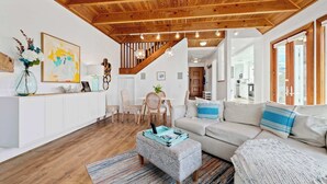 Un salón amplio con techo de madera, un conjunto de sofás, una mesa de centro y una escalera que sube a otro nivel.