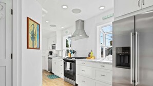 Una cocina moderna con armarios blancos, electrodomésticos de acero inoxidable y un amplio ventanal que proporciona luz natural.