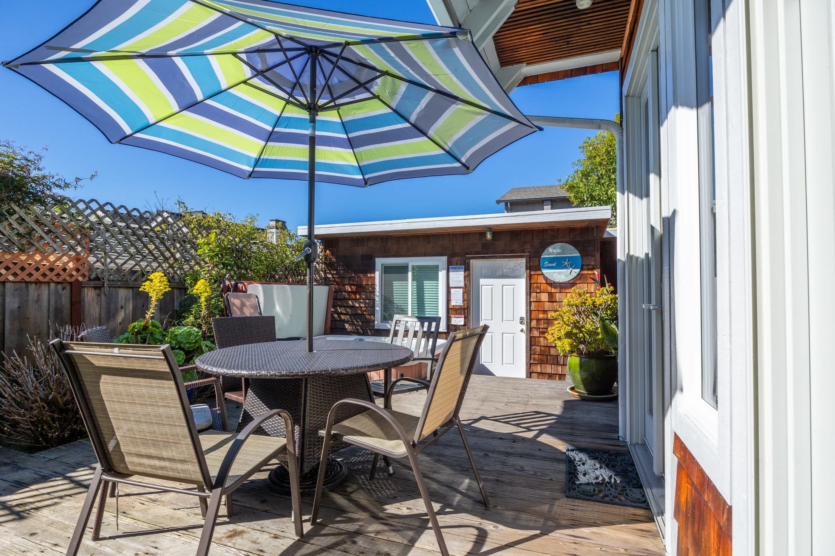 An outdoor patio with a round table and chairs, a striped umbrella, and a wooden fence.
