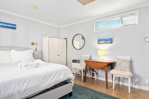 Une chambre d’hôtel avec un lit, un bureau, une chaise, un miroir et une fenêtre.