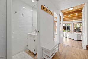 Une salle de bain moderne avec des carreaux de céramique blancs rectangulaires, un lavabo blanc et un plafond en bois.