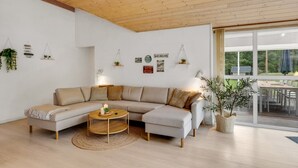 Een moderne woonkamer met een grote L-vormige bank, een ronde salontafel en een houten plafond.