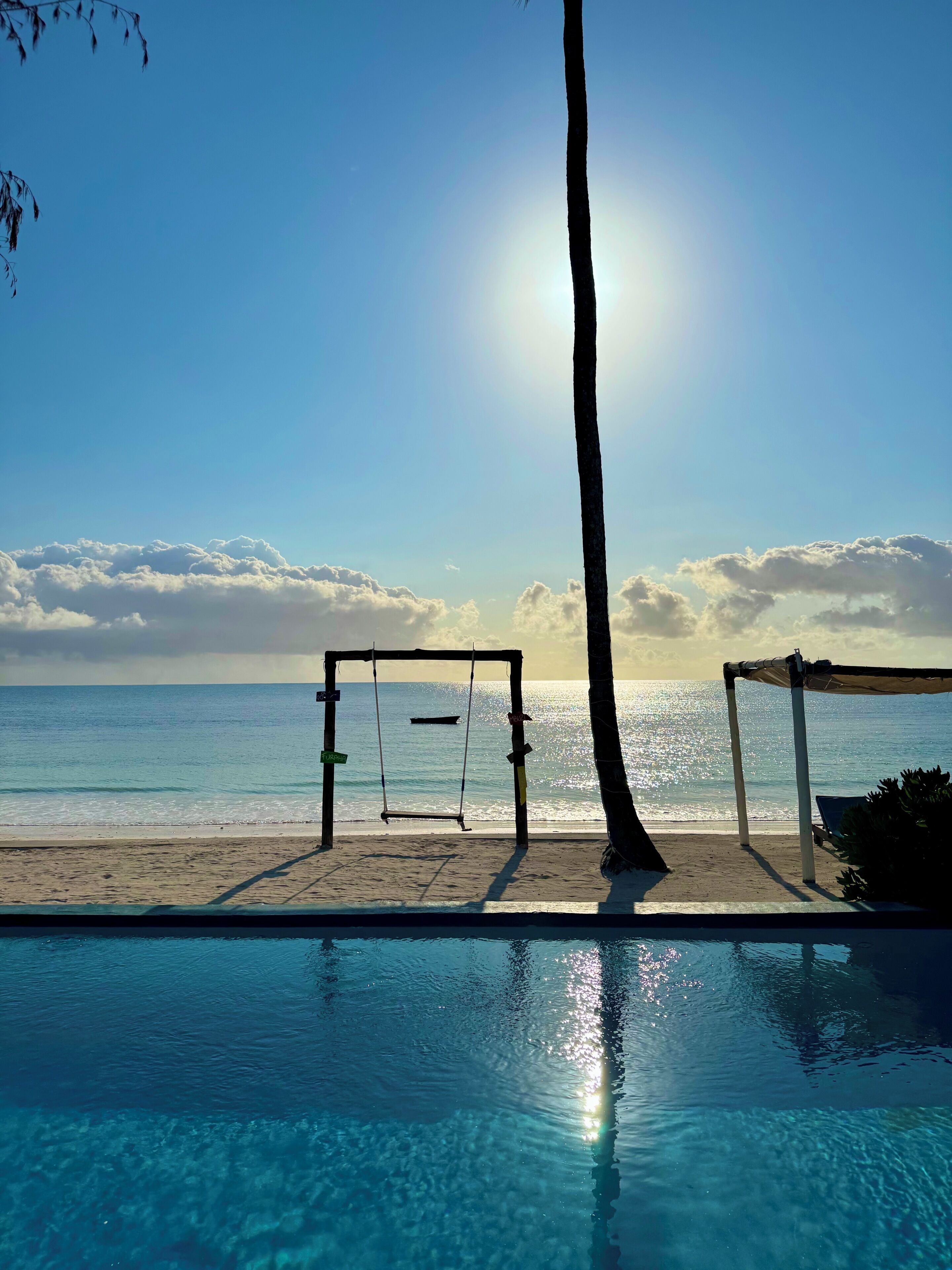 A clear sky, a swimming pool, a swing set, and a beach view.