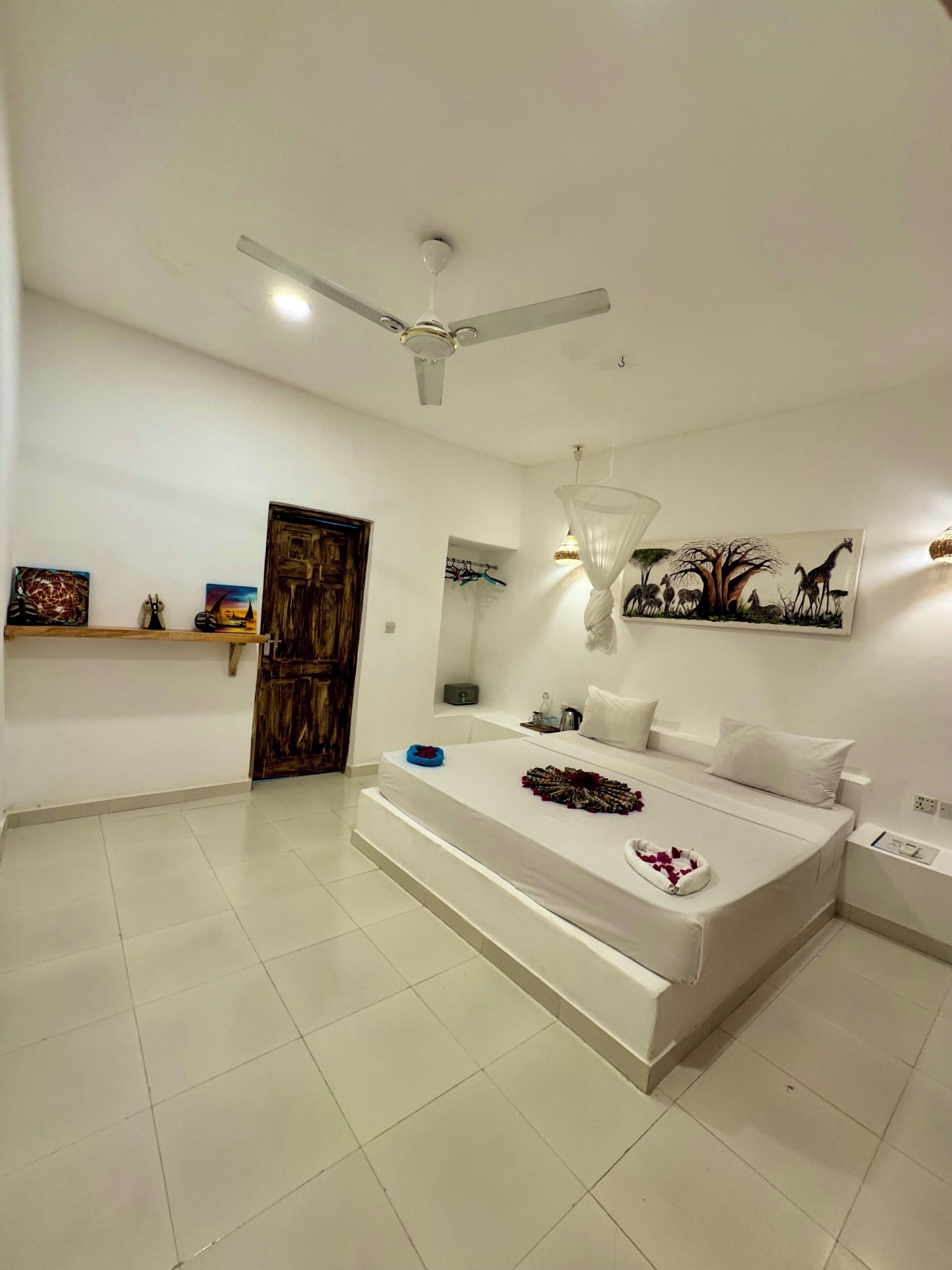 A modern bedroom with a bed, a ceiling fan, a painting, and a door.