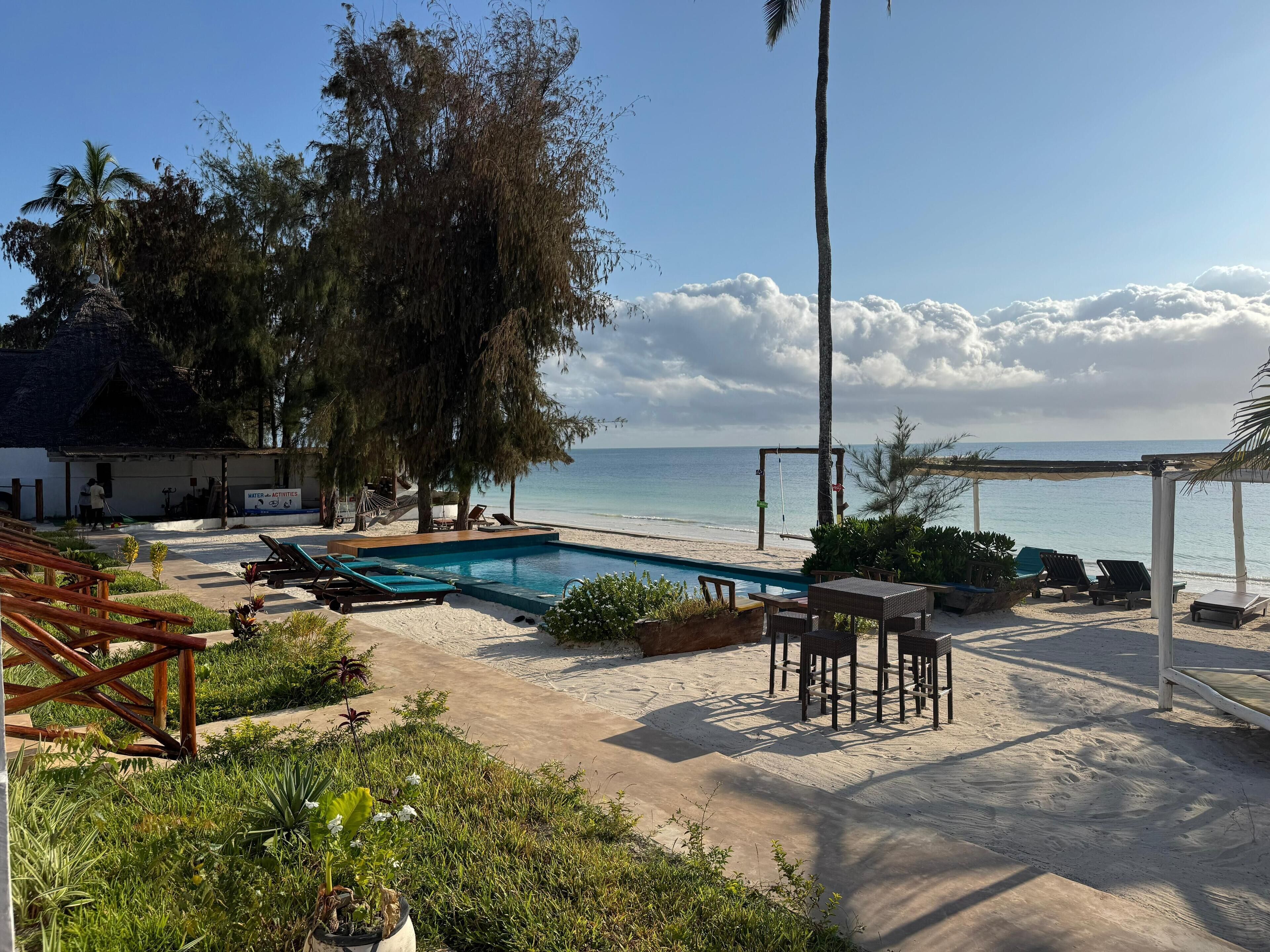 A pool area with lounge chairs and a pergola overlooking a beach.