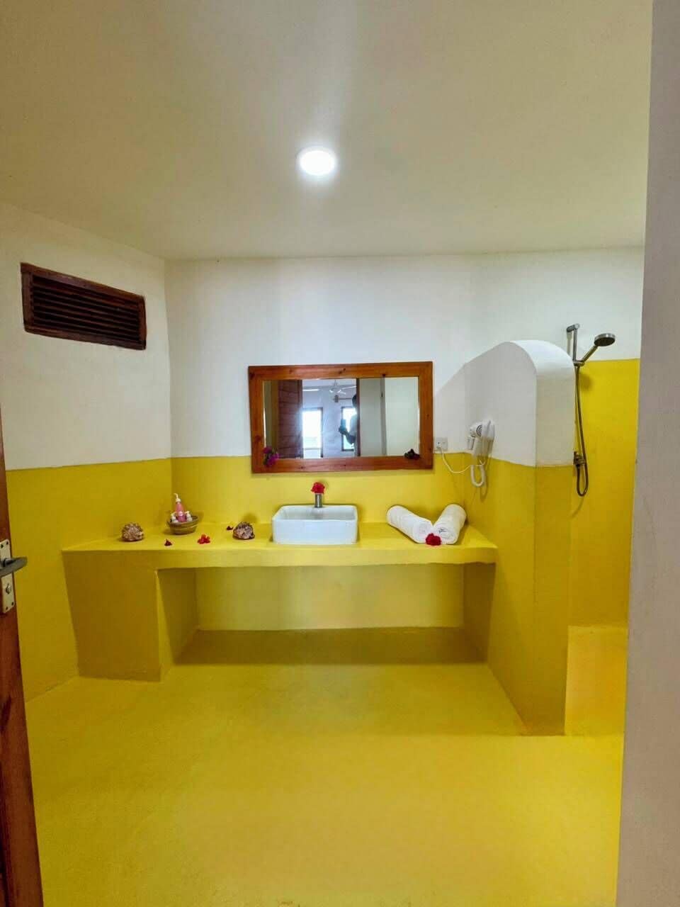 A bathroom with a yellow and white color scheme, a sink, a mirror, a shower, and a towel rack.
