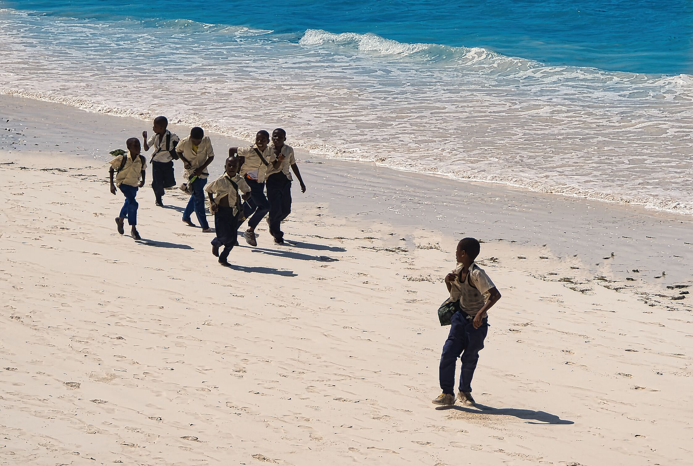 A sandy beach with footprints and a group of people in uniforms walking towards the water.