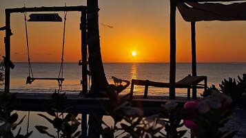 A beach scene with a swing set and a chair facing the sunset over the ocean.