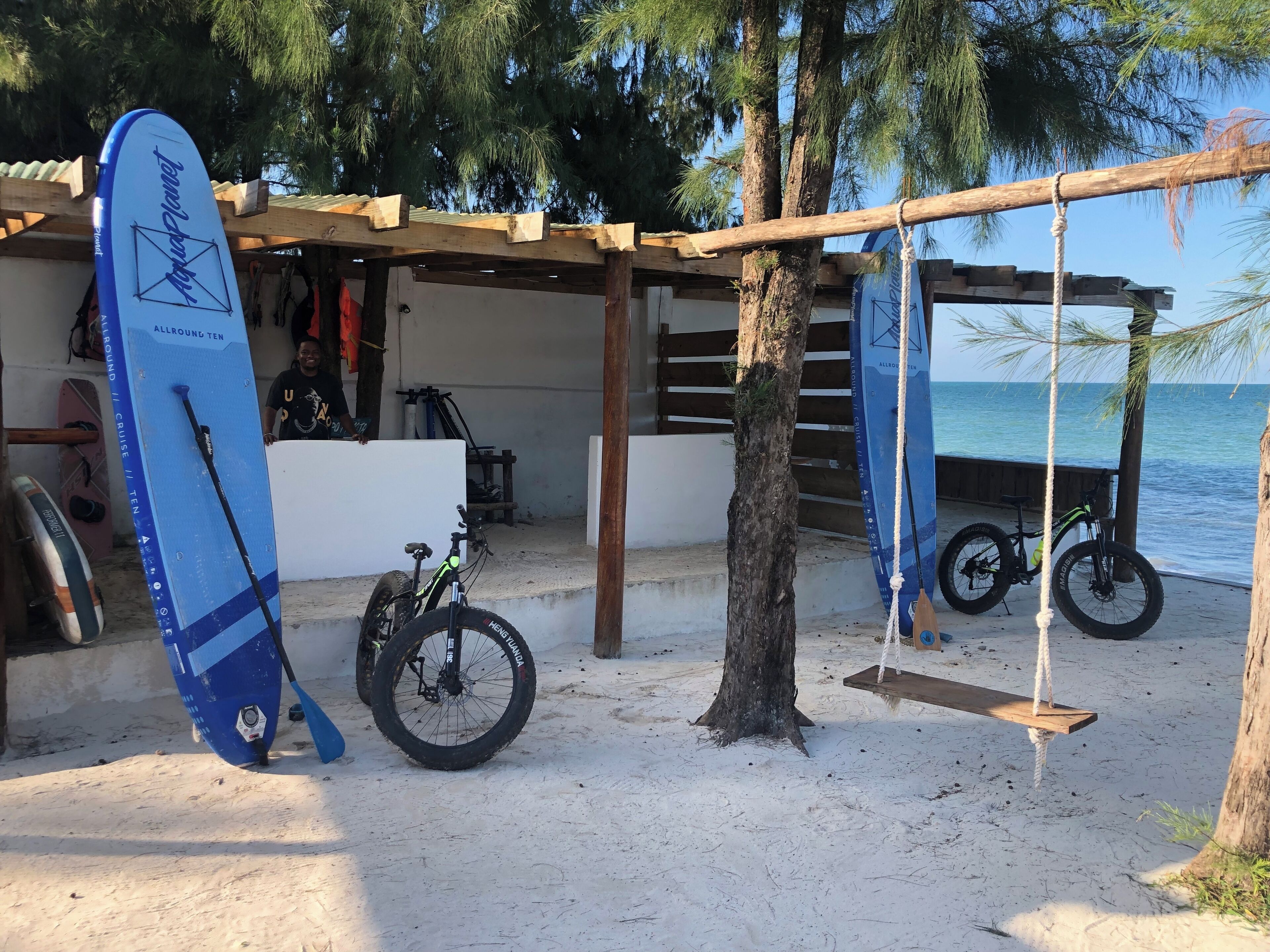 Un entorno costero con una estructura de madera, bicicletas y tablas de surf.