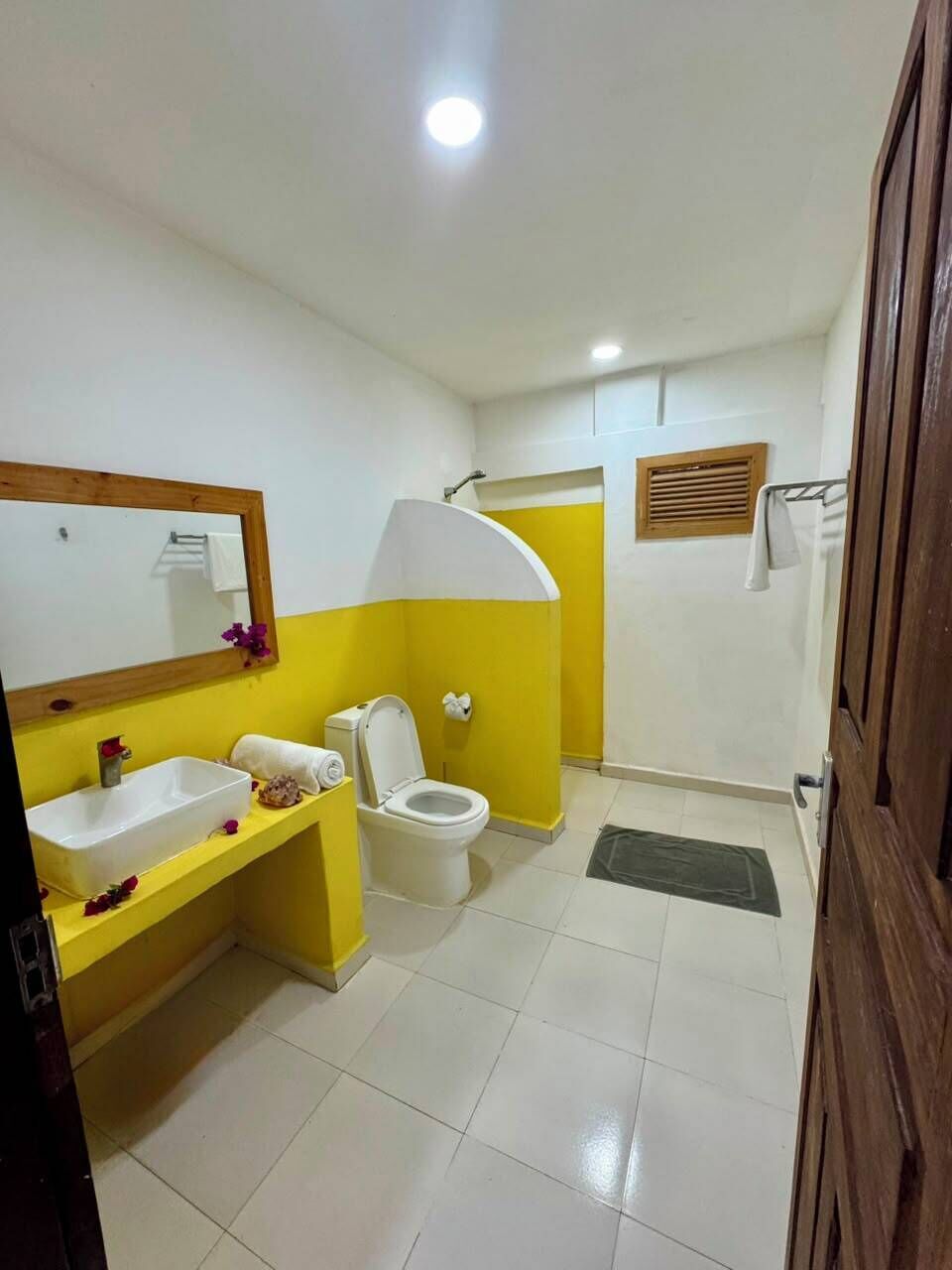 Un baño con tocador amarillo, lavabo blanco, inodoro y zona de ducha.