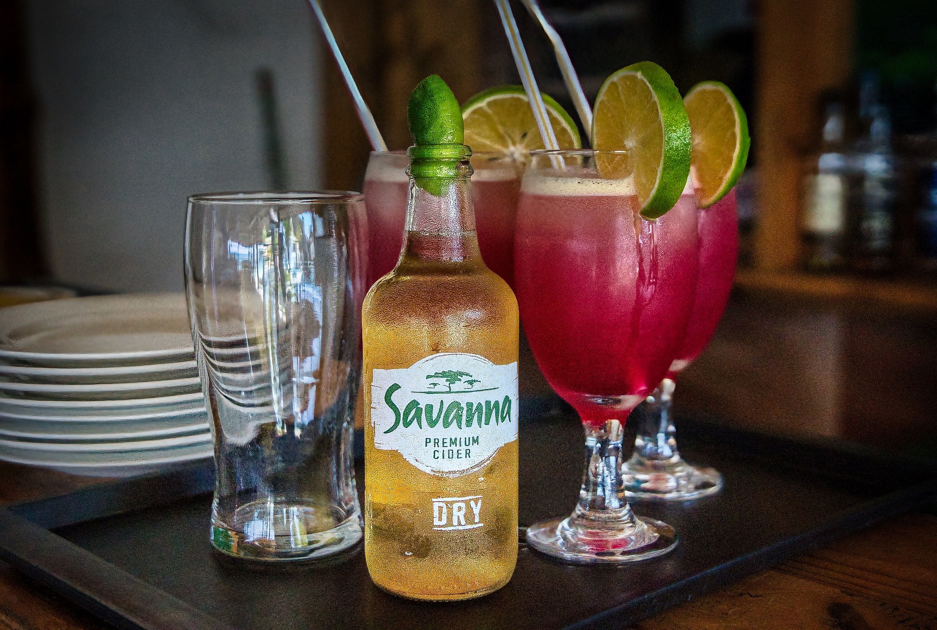A bottle of Savanna Premium Cider and two glasses of a red beverage with lime slices.