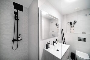 A modern bathroom with a shower, sink, toilet, and a large mirror.