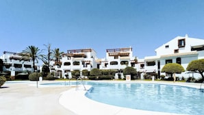 Een resort met een zwembad, witte gebouwen met balkons en palmbomen.