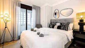Een hotelkamer met een groot bed, een bureau en een stoel. Er is een raam met gordijnen, een lamp en een spiegel aan de muur.