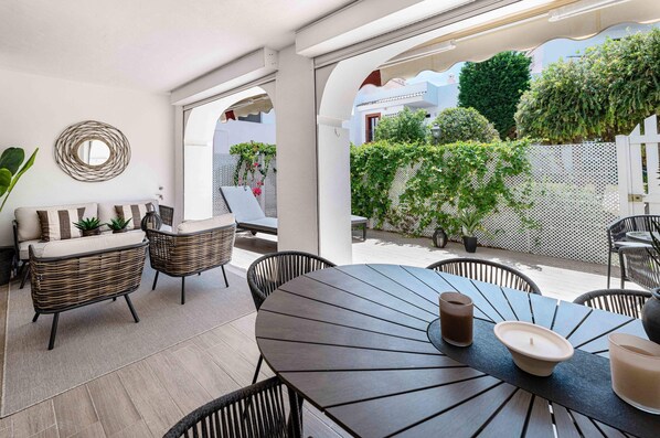 Un espace extérieur aménagé en terrasse, avec une table ronde, des chaises en osier et un banc rembourré.