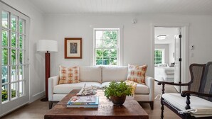 A living room with a white sofa, a wooden coffee table, and a chair. There is a window with a view of greenery outside. - Luxury condo with views & amazing location! Minutes to town and beaches (Kennebunkport)
