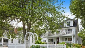 A two-story house with a front porch, a white picket fence, and a large tree in the background. - Luxury condo with views & amazing location! Minutes to town and beaches (Kennebunkport)
