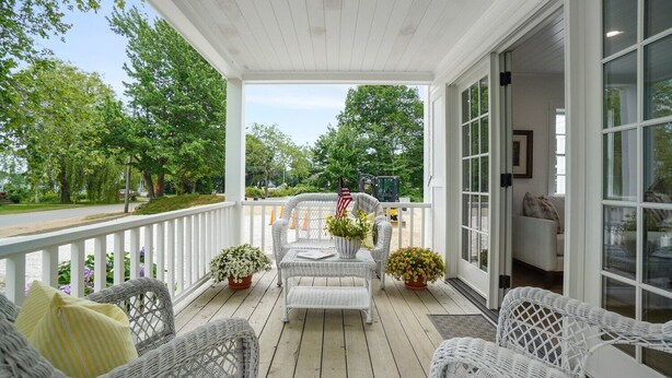 A covered porch with wicker furniture, potted plants, and a view of the street and greenery. - Luxury condo with views & amazing location! Minutes to town and beaches (Kennebunkport)
