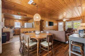 Un intérieur en bois avec une table de salle à manger ronde, des chaises, un canapé et un téléviseur.