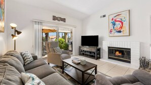 A modern living room with a sectional sofa, a flat-screen TV, a fireplace, and a ceiling fan. - Near Coachella Two Bedroom Two Bath Condo, Steps from the Pool & Spa, Desert Falls CC (Palm Desert)