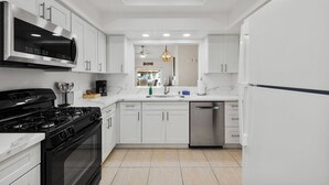 A modern kitchen with white cabinetry, a black stove, stainless steel appliances, and a tiled floor. - Near Coachella Two Bedroom Two Bath Condo, Steps from the Pool & Spa, Desert Falls CC (Palm Desert)