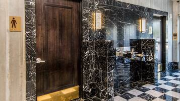 A hotel lobby with a checkered floor, a marble wall with a door, and a men's restroom sign.