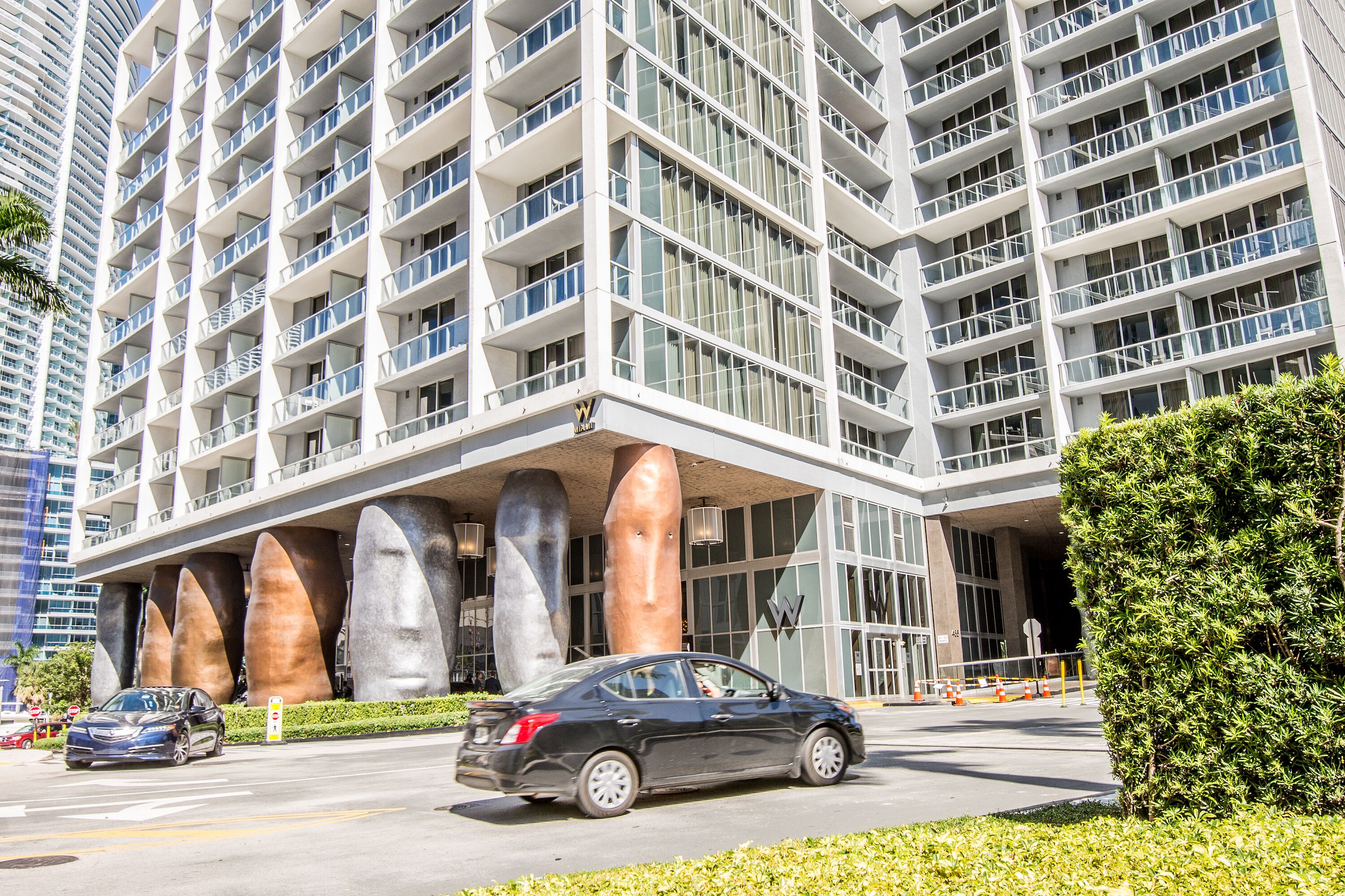 A modern hotel with a multi-story structure, large windows, and a prominent entrance with a unique architectural design featuring large, curved pillars.