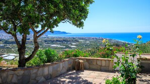 A stone pathway leading to a terrace overlooking a coastal landscape with a tree and flowering plants.