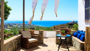 A patio with wicker furniture, a round table, and a view of the sea and landscape.