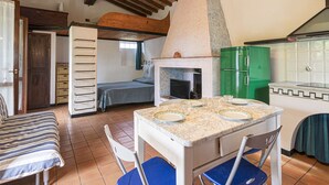 Een compacte keuken met een stenen oven, een groene koelkast en een eethoek met een marmeren tafel.