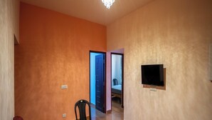 A living room with orange walls, a chandelier, a TV mounted on the wall, and a door leading to another room. - Hill Lock Mist (Kodaikanal)
