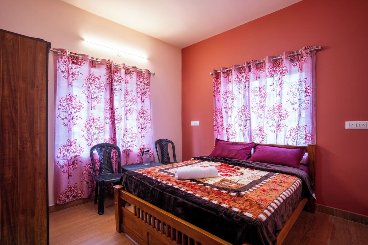 Un dormitorio con cama, dos sillas y cortinas estampadas con motivos florales.